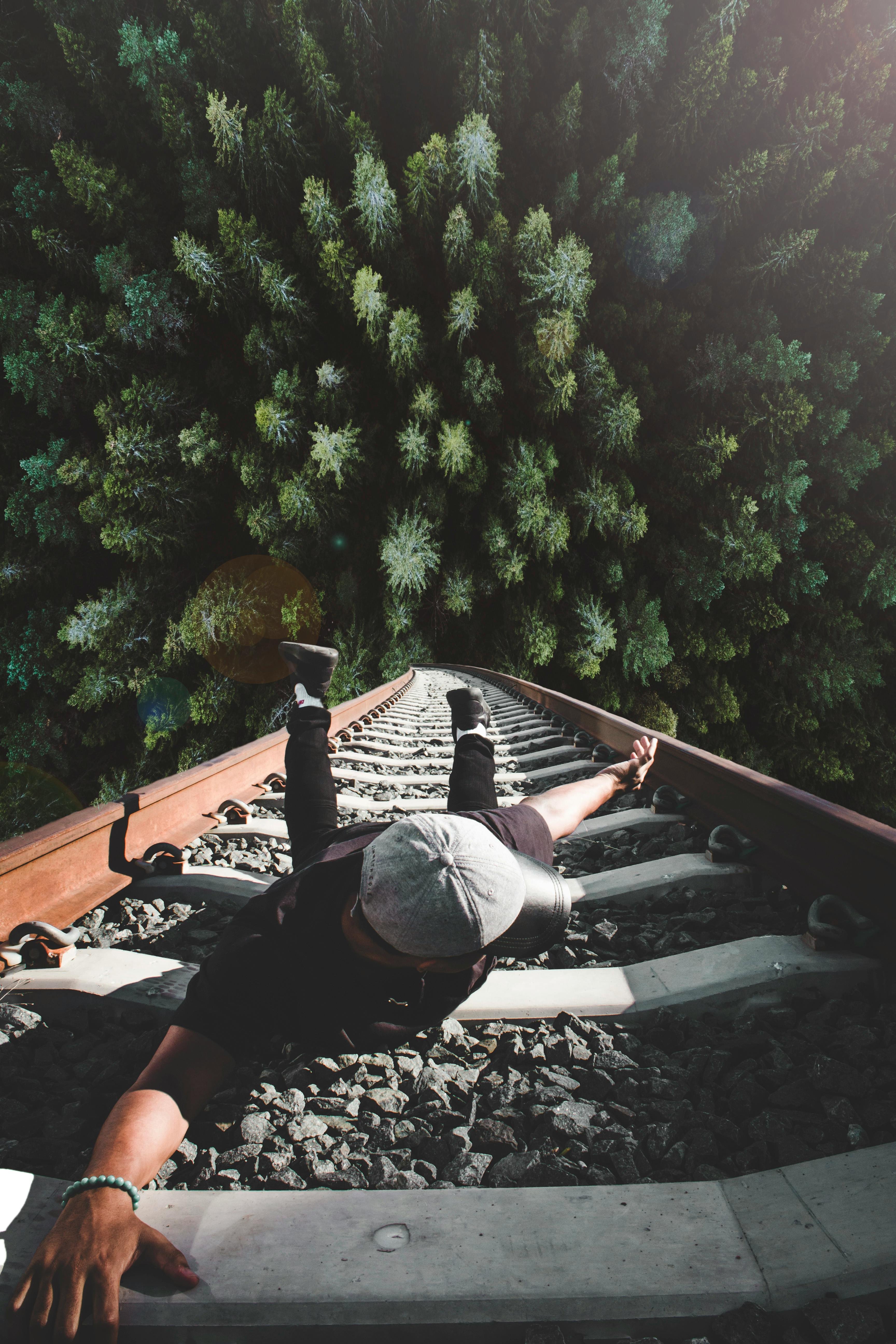 Man Lying on Railway Tracks Above Forest